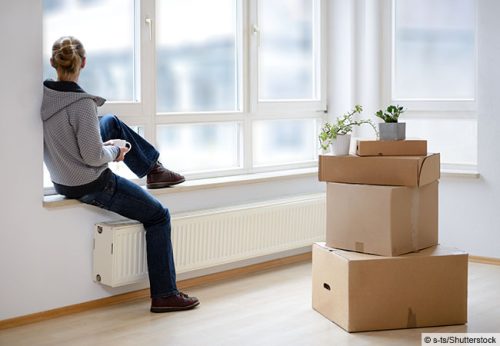 Eine Person sitzt am Fenster und schaut raus. Neben ihr sind Umzugskartons © s-ts/Shutterstock