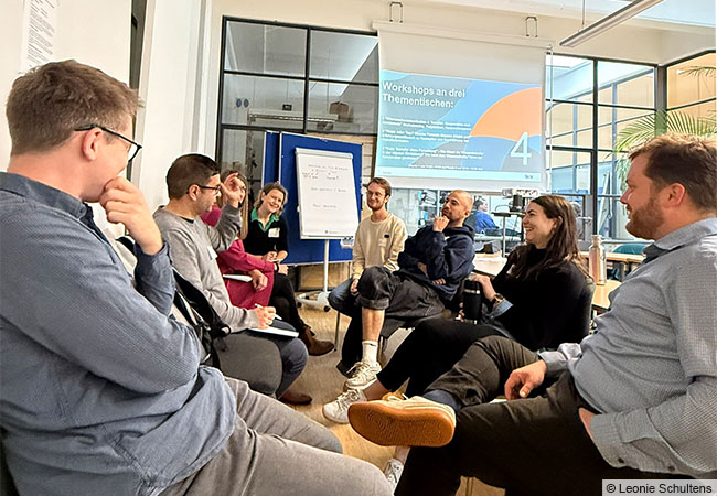 Menschen sitzen in einem Stuhlkreis zusammen und unterhalten sich angeregt. © Leonie Schultens