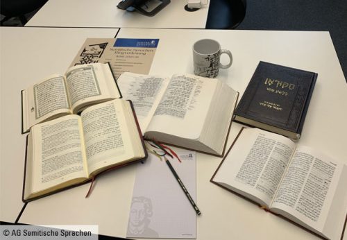 Im Uhrzeigersinn ab dem geschlossenen Buch handelt es sich dabei um: 1. Koran in Hebräisch, 2. Bibel auf Arabisch, 3. Peshitta = Bibel in Syrisch-Aramäisch (Syriac), 4. Koran, 5. In der Mitte: Hebräische Bibel. © AG Semitische Sprachen
