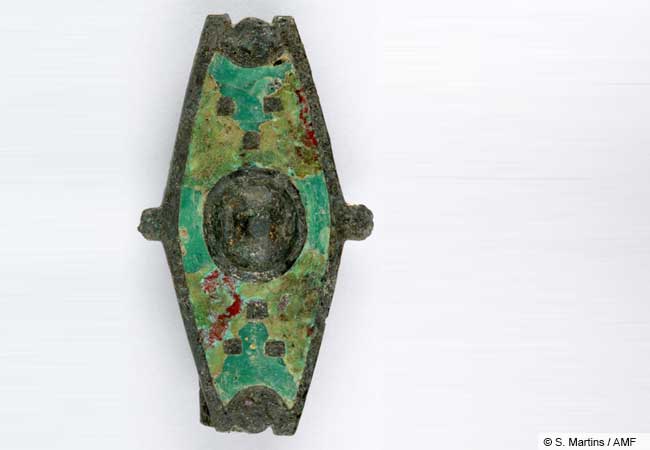 One of the more unusual brooches from the cult district: a hexagonal bronze garment clasp whose shape and enamel decoration recall Roman military shields. (© S. Martins / AMF).