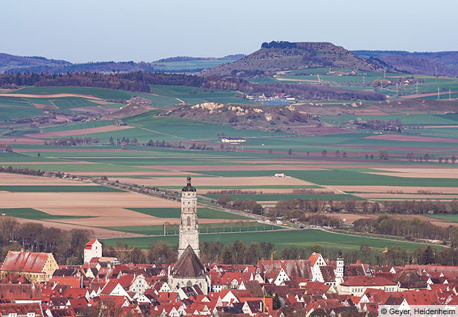 Die mittelalterliche Stadt Nördlingen mit dem Kirchturm Daniel der St.-Georgs-Kirche, im Hintergrund (im Westen) der mächtige Ipf mit seinen bronze- und eisenzeitlichen Befestigungen. (© Geyer, Heidenheim)